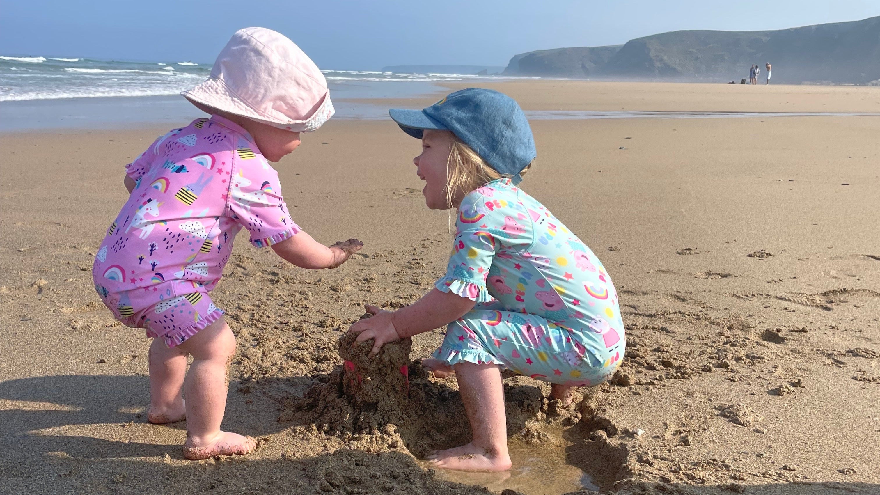Two children playing in the sand on a beach with a clear sky.