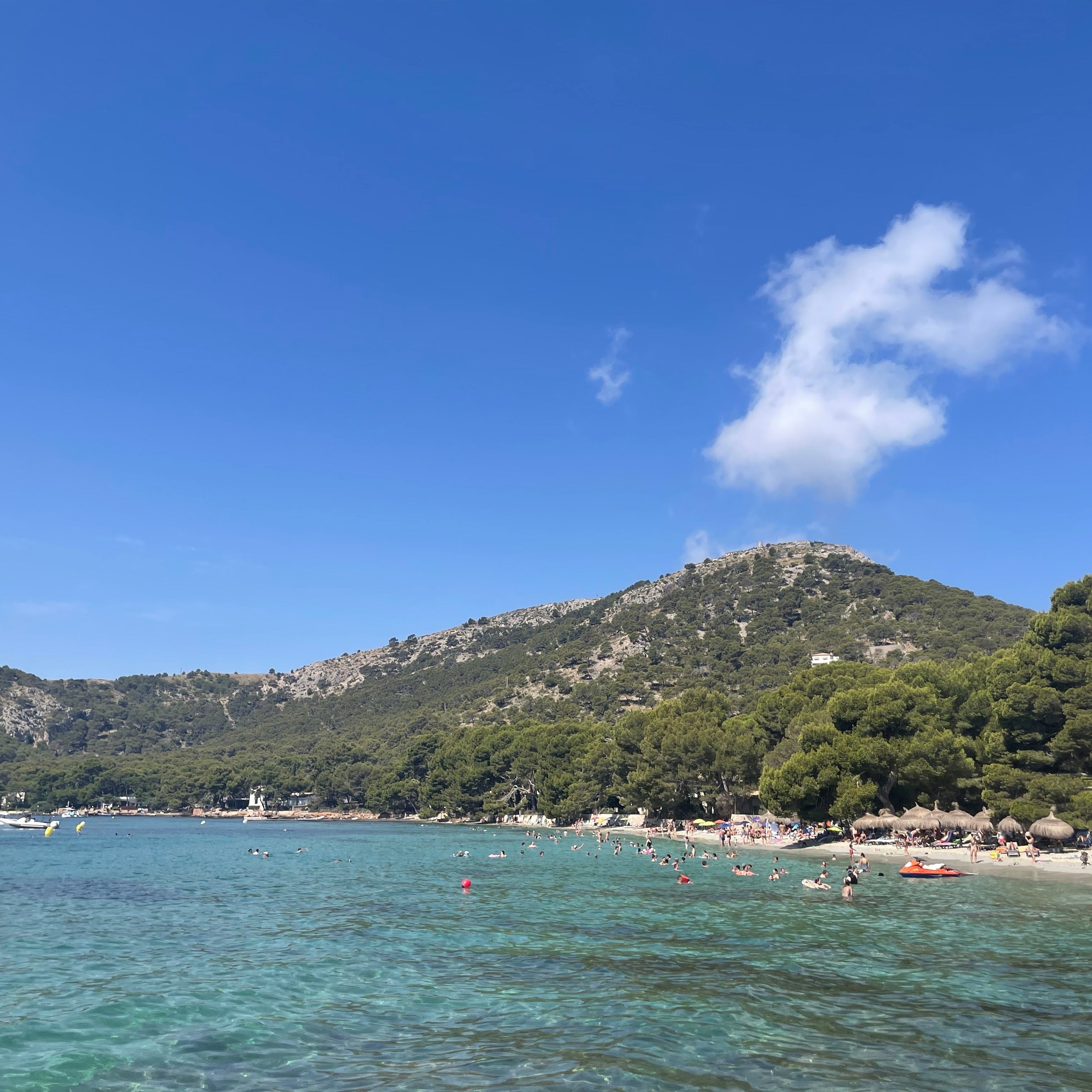 Tropical beach with clear blue water, green mountains, and a few people enjoying the sun.
